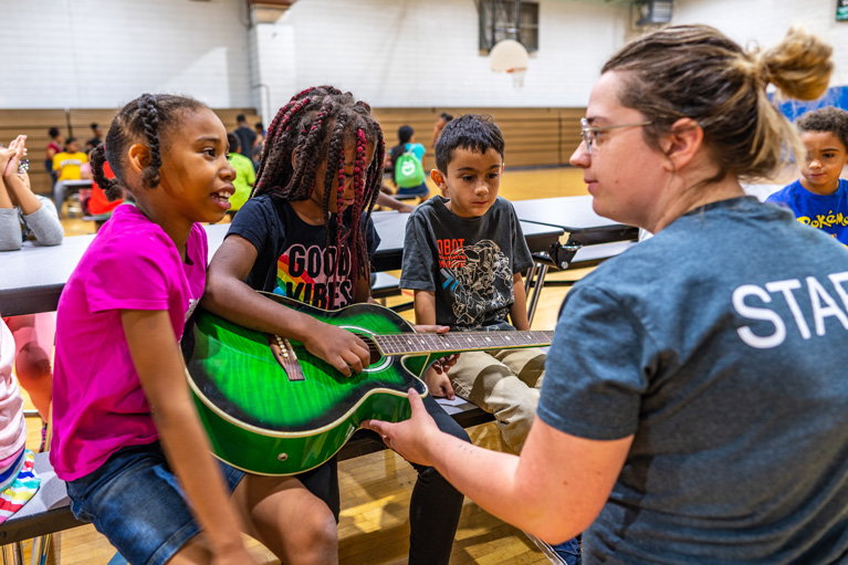 Youth Development Professional and 3 Club kids playing guitar
