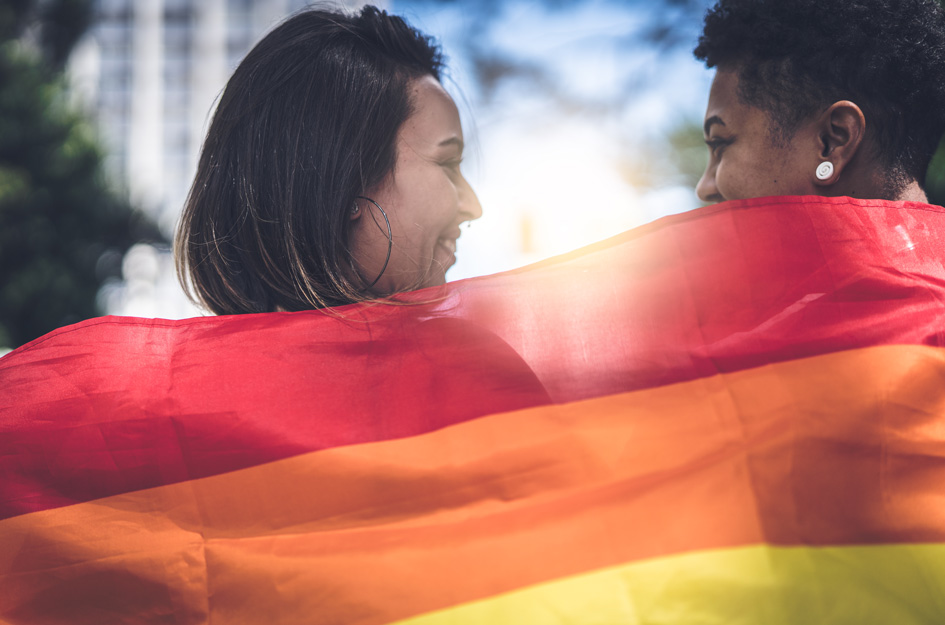 2 young women wrapped in rainbow flag