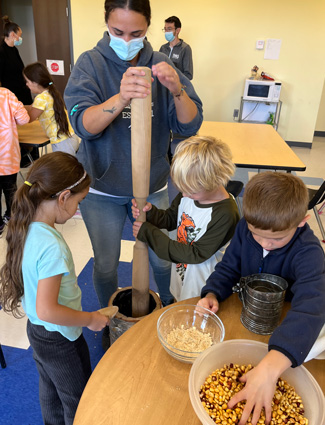 Youth and teacher using their botaagan to grind corn kernels