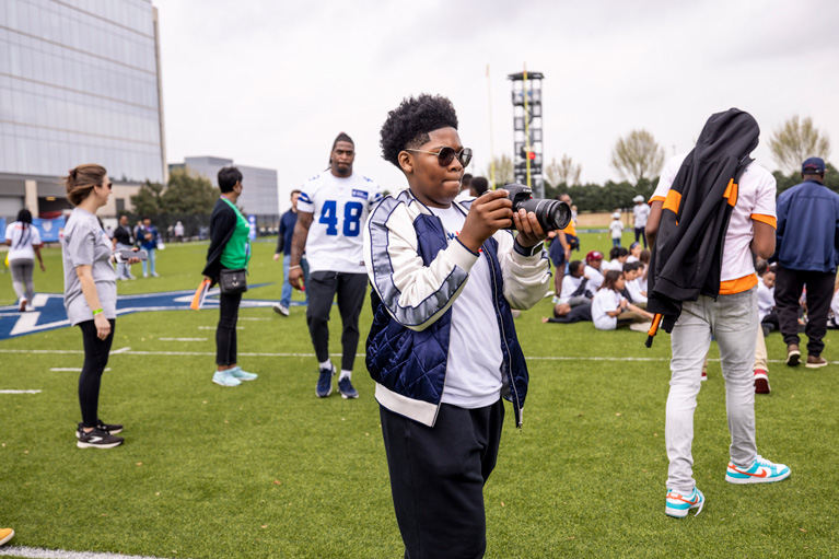 Isaac behind the scenes capturing action shots featuring Greater Dallas Boys & Girls Club youth at “Beyond the Field: Tacking STEM” event